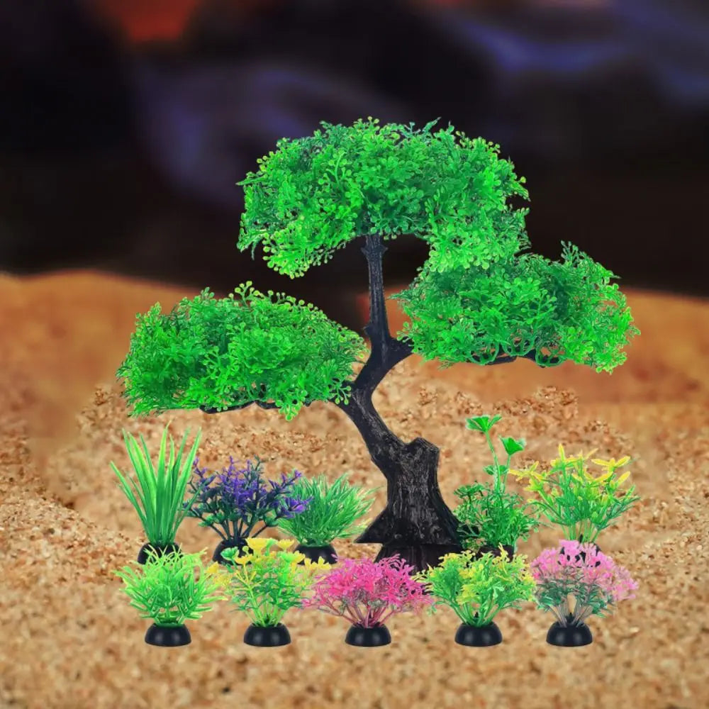 An artificial plastic bonsai tree surrounded by an assortment of colorful, small aquatic plants on a sandy background.
