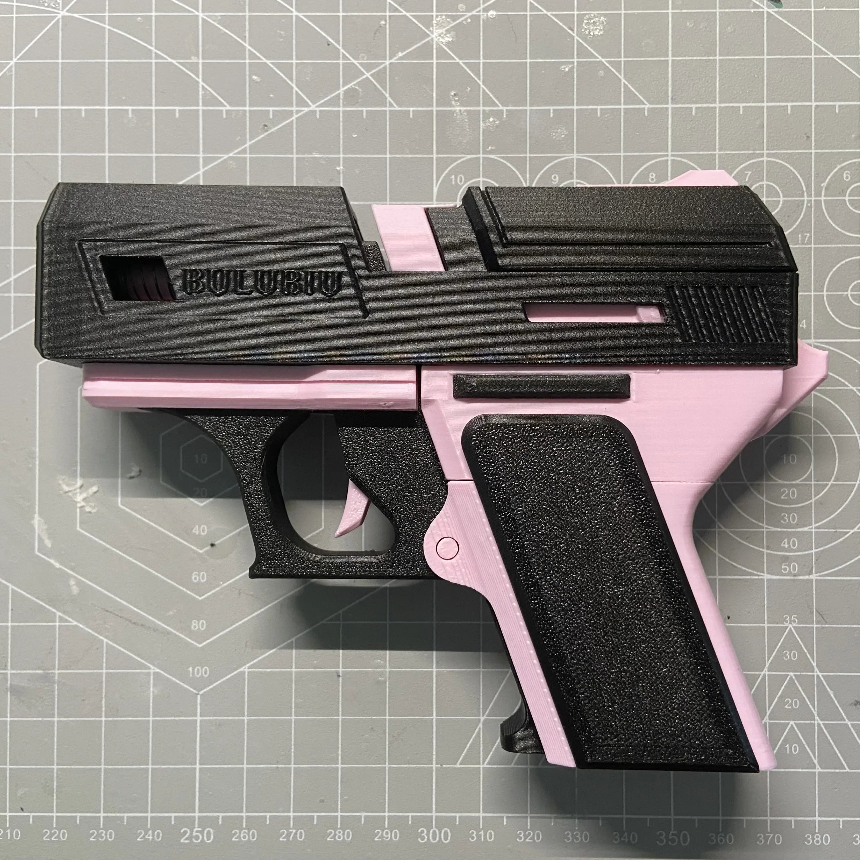 Black and pink 3D-printed gun-style AirPods case on a cutting mat.