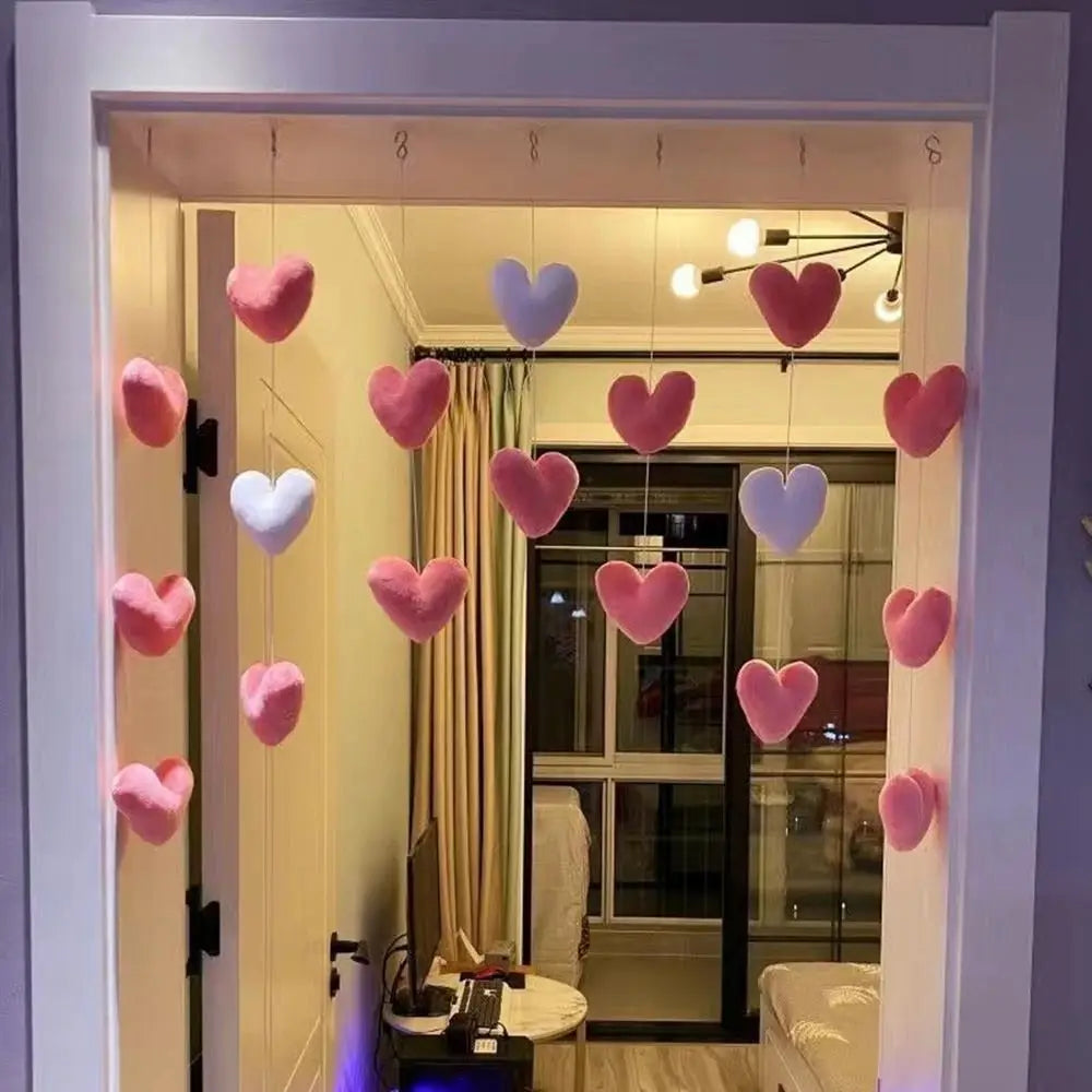 A decorative doorway hanging featuring plush pink and white hearts suspended on strings.