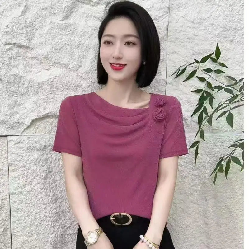 A woman wearing a short-sleeved, berry-pink top with a draped neckline and two small floral accents on the shoulder.