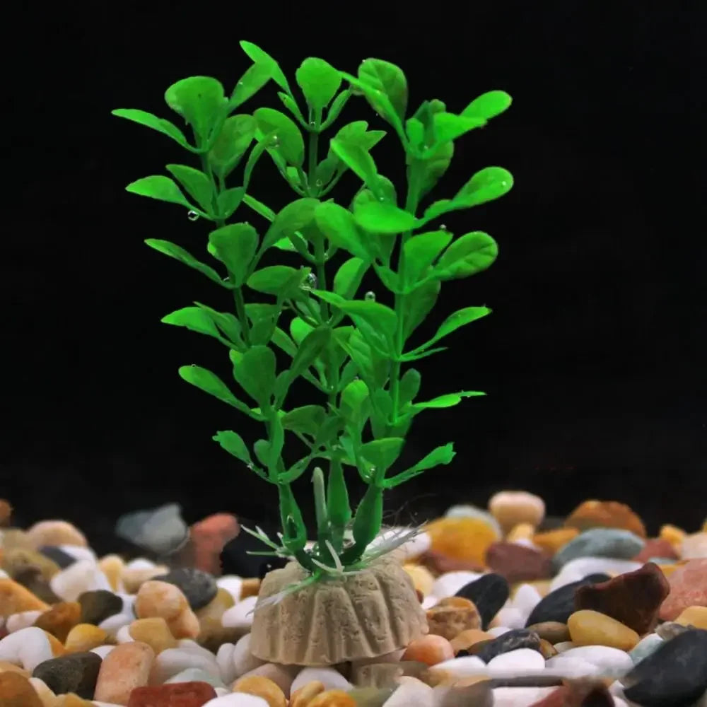 Bright green plastic aquarium plant with small leaves, set in a textured tan base on colorful gravel against black.