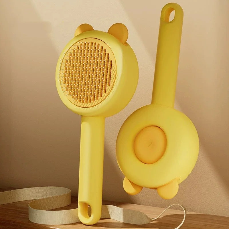 Two yellow pet grooming brushes with bear-ear detailing and long handles, shown from the front and back.