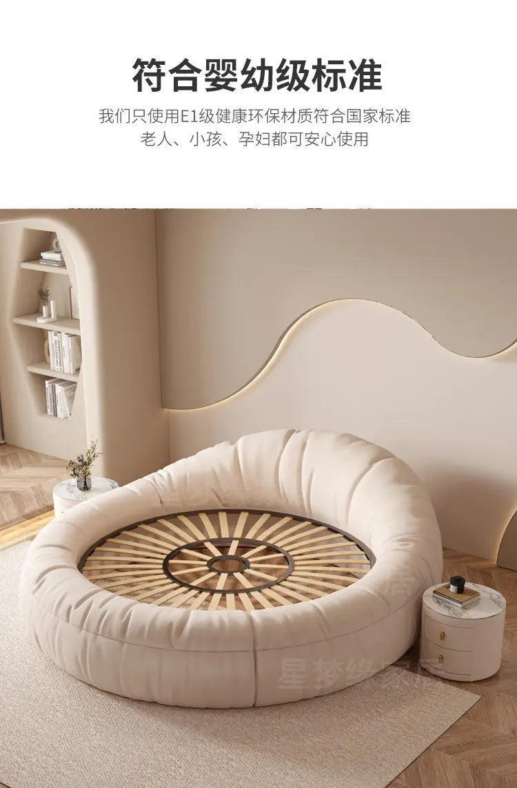 Modern circular cream fabric bed frame with wooden slatted base in a minimalist bedroom setting.