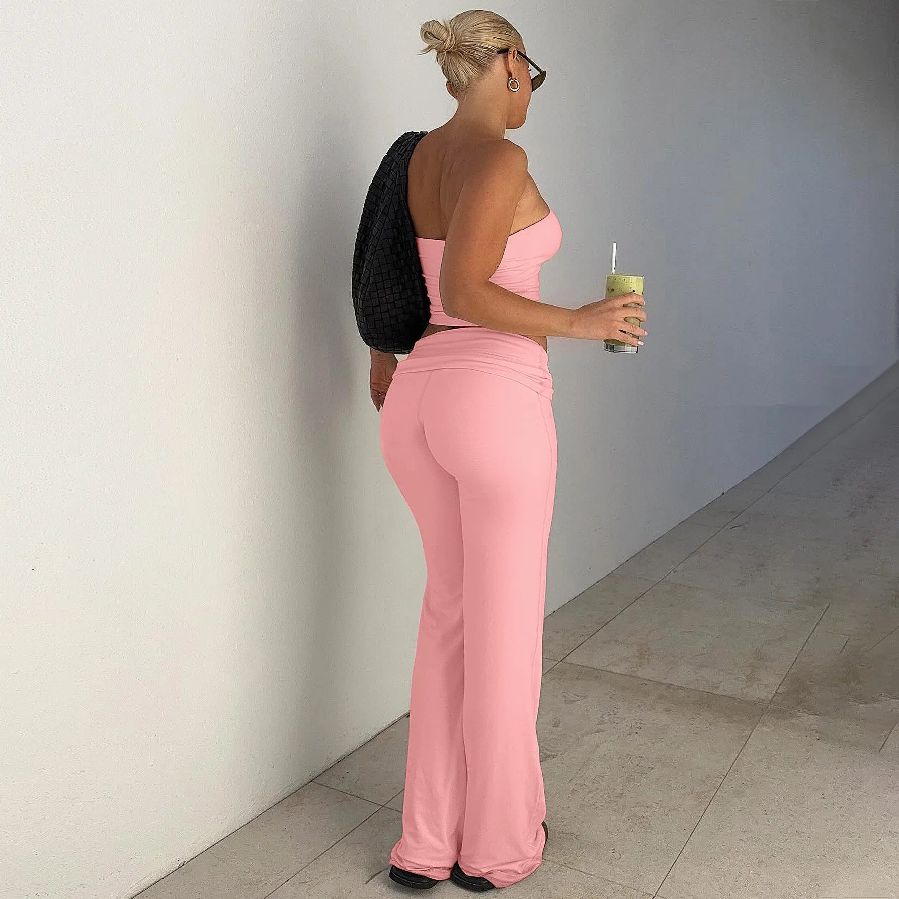 Woman wearing a light pink, two-piece set featuring a strapless crop top and matching low-rise flared trousers.