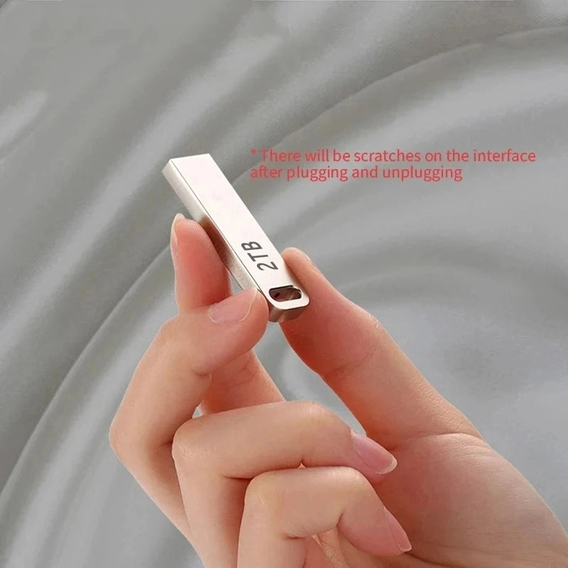 A sleek, silver 2TB portable USB flash drive being held between fingers, featuring a slim, minimalist metal design.