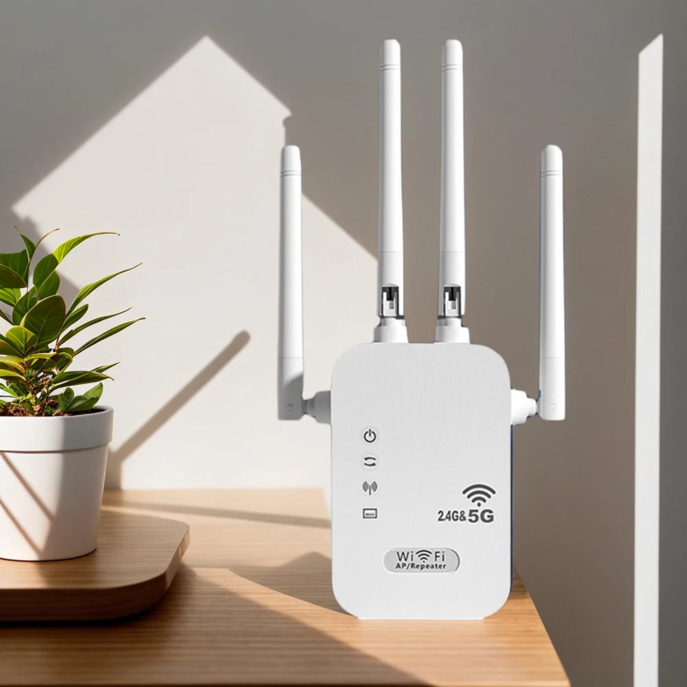 White dual-band WiFi repeater with four antennas on a wooden desk next to a potted plant.
