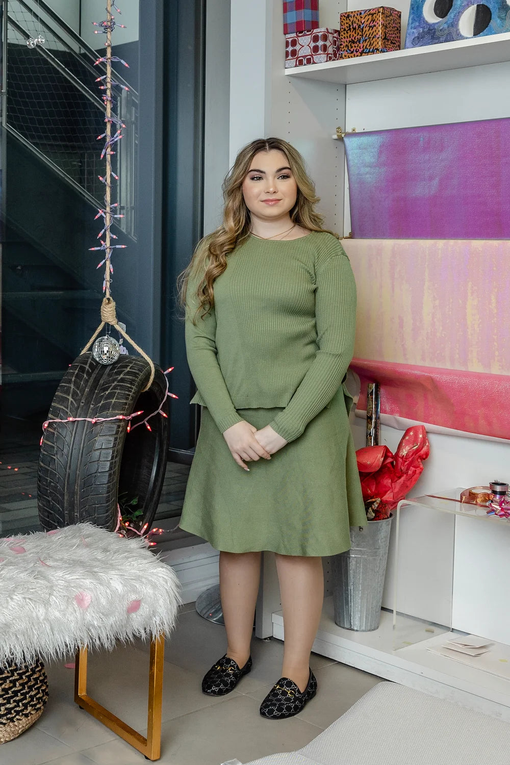 A woman wearing a sage green long-sleeved, ribbed knit top and a matching A-line skirt.