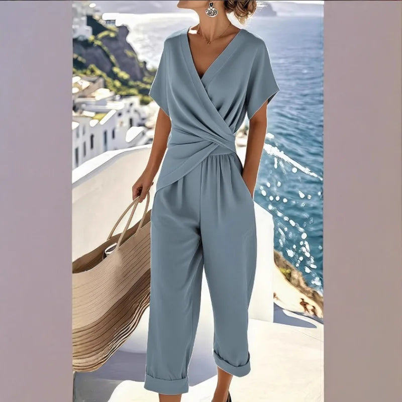 Dusty blue jumpsuit with V-neck, short sleeves, wrapped waist detail, and cuffed cropped trousers.