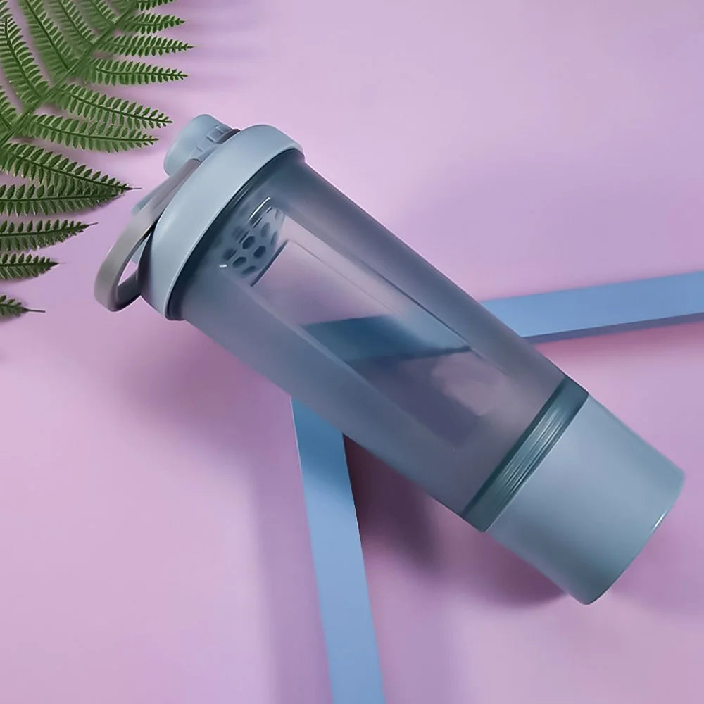 Grey plastic protein shaker bottle with a carry handle and internal mixing grid on a purple background.