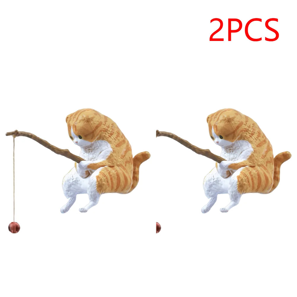 Two small, orange tabby cat ornaments for an aquarium, each holding a toy fishing rod with a hanging bauble.