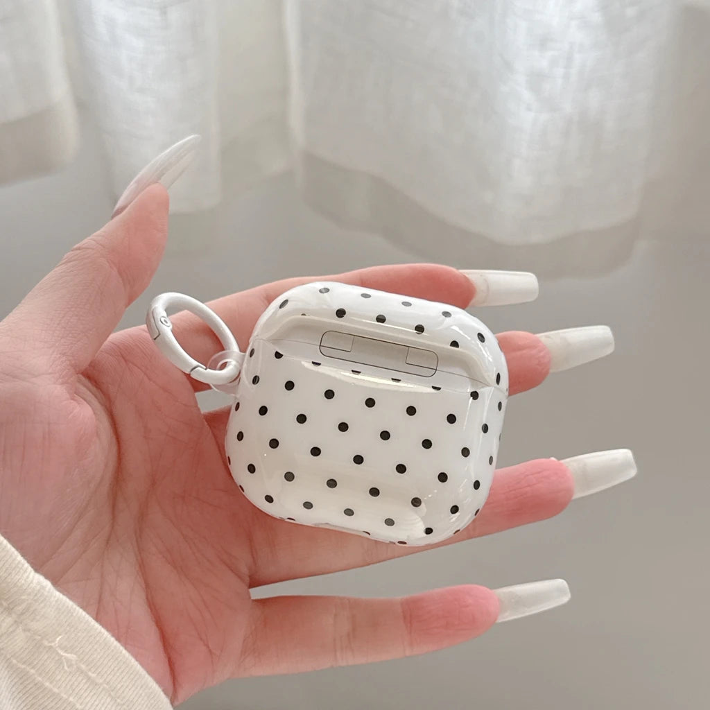 White and black polka dot clear AirPods case with a white carabiner clip, held in a hand.