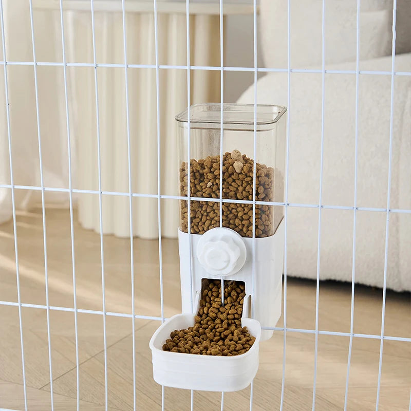 Clear and white wall-mounted pet food dispenser hanging on a wire cage, filled with brown dry kibble.