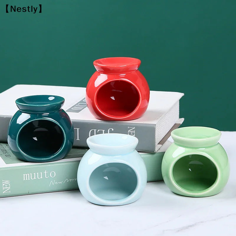 Four colourful, round ceramic oil burners in red, dark green, light blue, and pastel green sitting on books.
