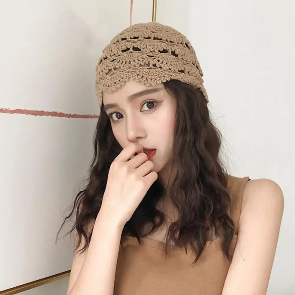 A woman wearing a beige hollow-knit crochet beanie with an intricate scalloped edge.