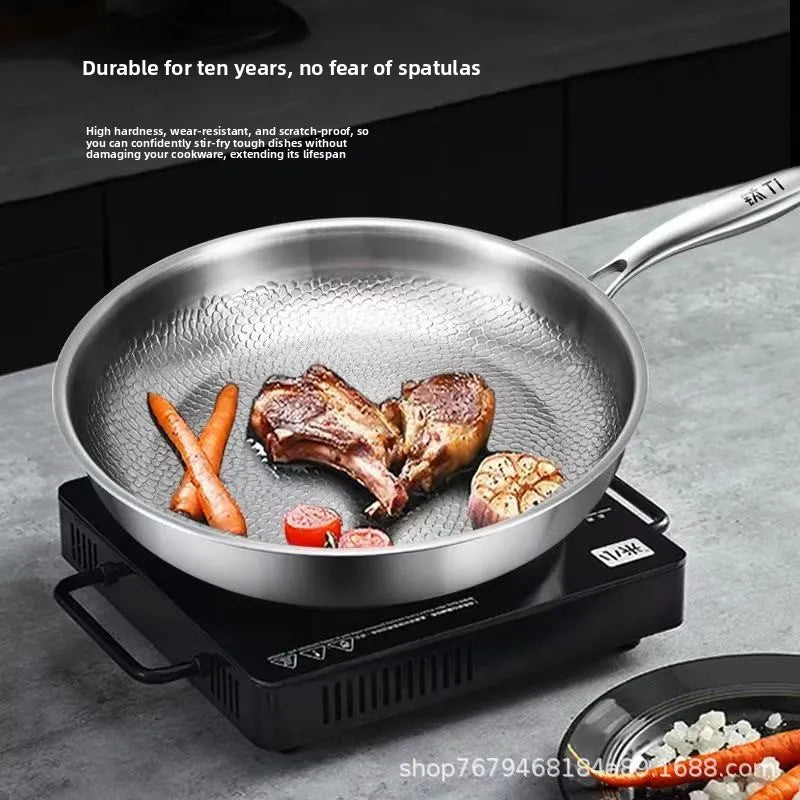 A stainless steel frying pan with a honeycomb textured interior sits on a portable stove, containing cooked chops and vegetables.