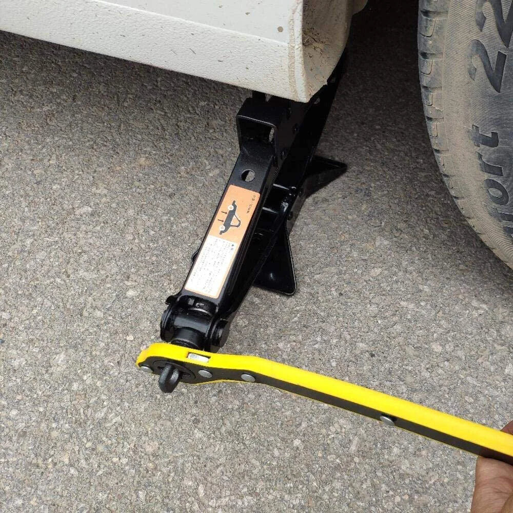 Black 2.5T scissor jack supporting a car with a yellow hand crank wrench attached on asphalt.