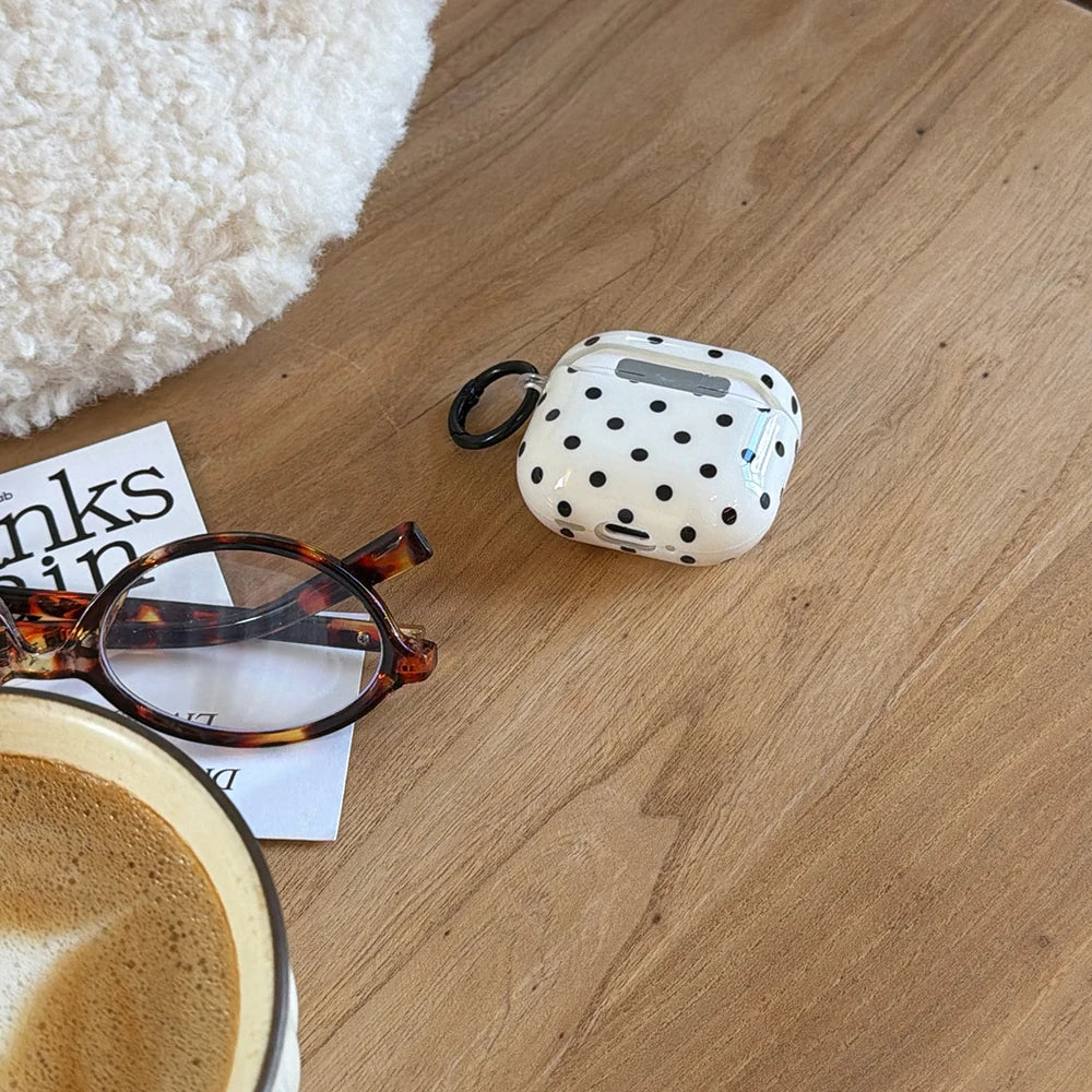 White polka dot protective AirPods case with black keychain attachment, set on a wooden table.