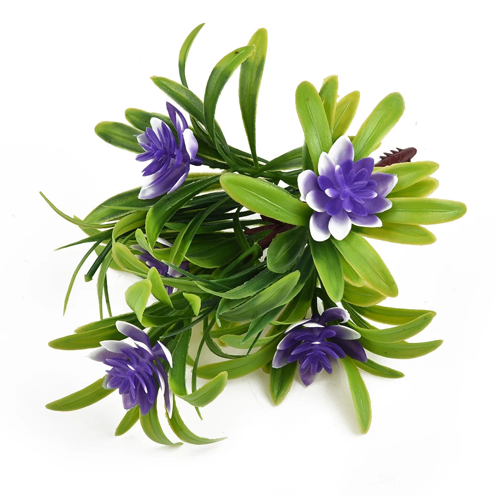 Artificial bunch of fake green grass with small, purple and white flower blossoms on a white background.