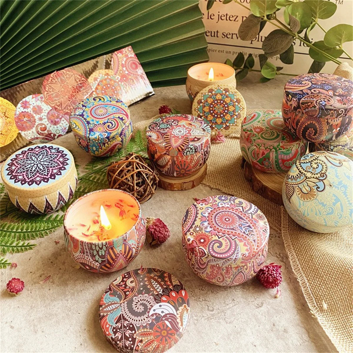 Group of round metal candle tins featuring colourful bohemian mandala and paisley patterns, some lit and open.