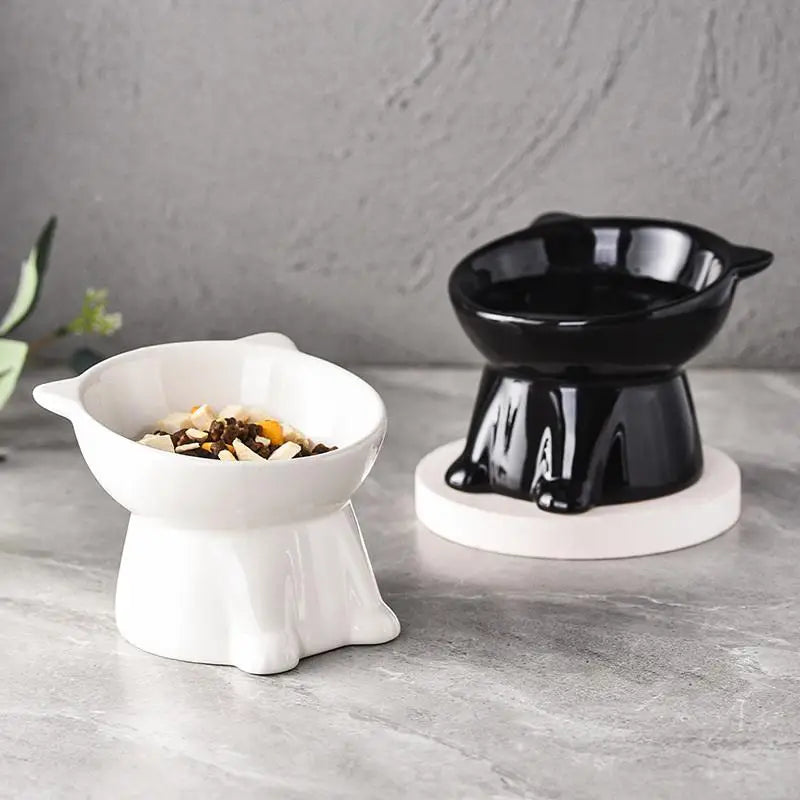 Two tilted ceramic pet bowls, one white and one black, designed for neck comfort on a grey surface.