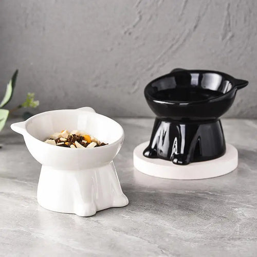 Two tilted ceramic pet bowls, one white and one black, designed for neck comfort on a grey surface.