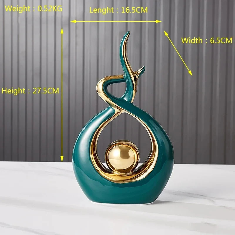 A modern, abstract dark teal ceramic ornament with gold trim and a central gold sphere on a white surface.