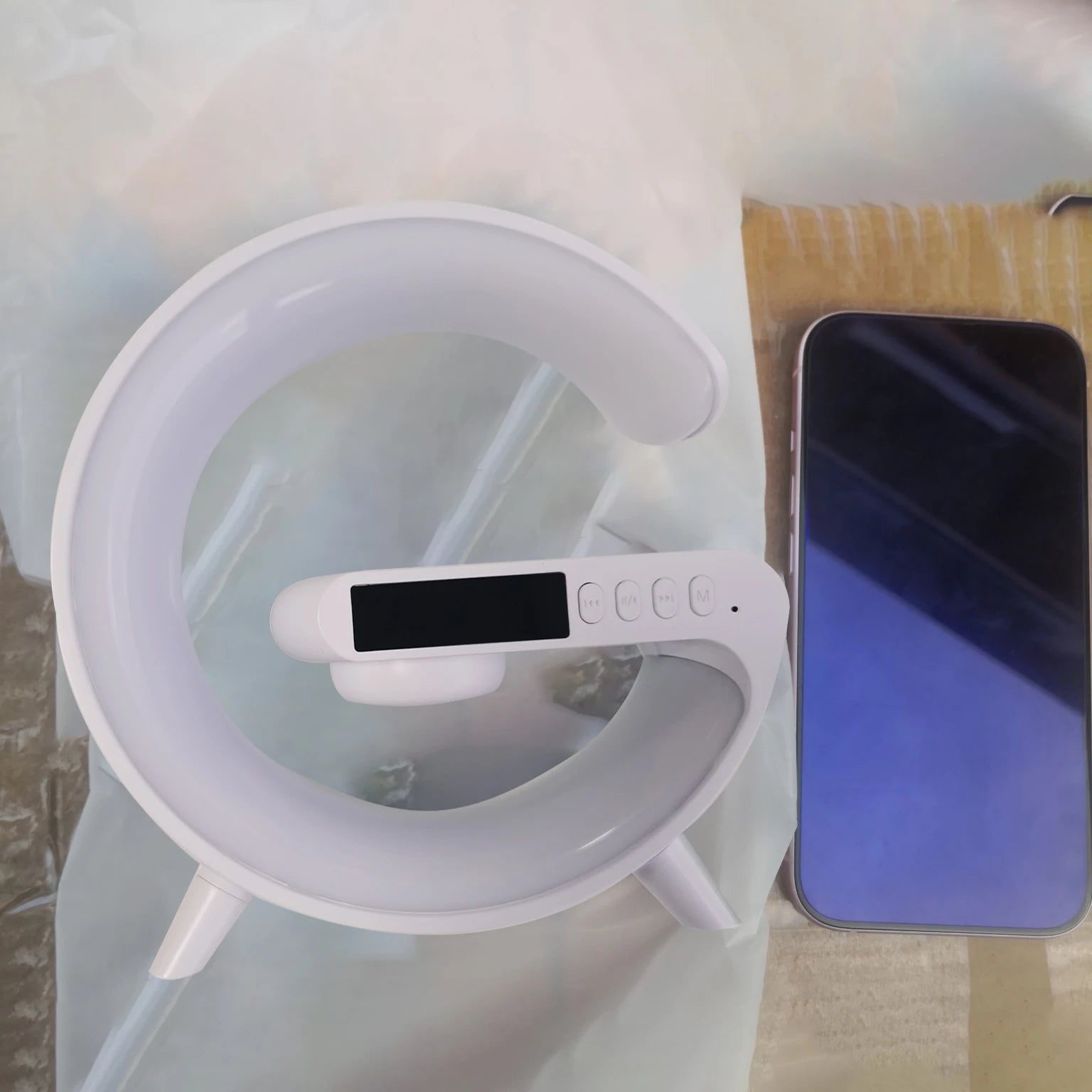 White G-shaped wireless speaker and charging station with integrated RGB night light and control buttons next to a phone.