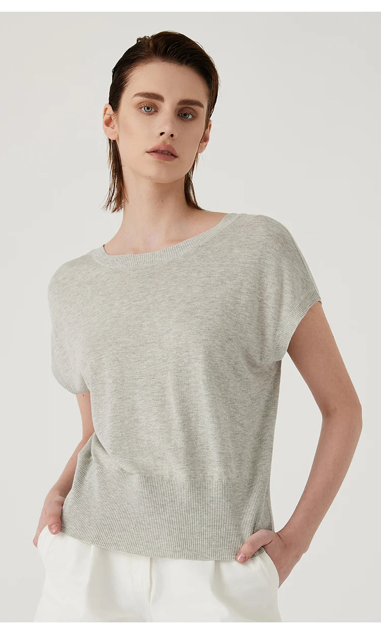 Model wearing a light grey, short-sleeved knitted top with a round neckline and ribbed hem.
