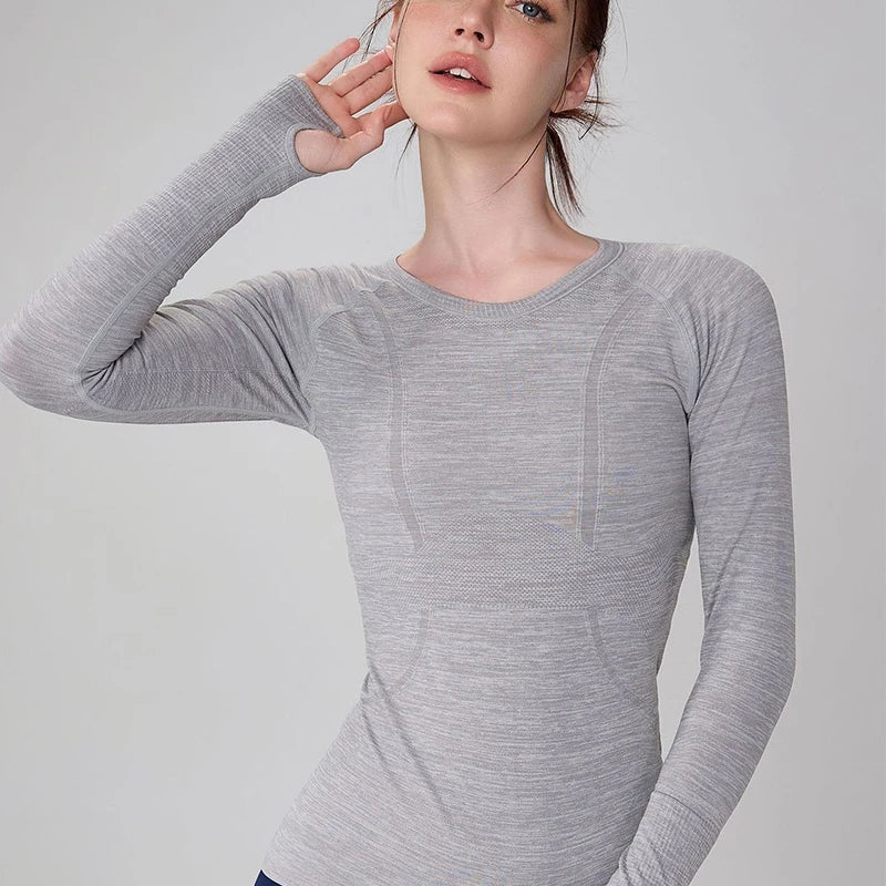 Grey long-sleeve seamless activewear top with a crew neck and thumbhole cuffs on a model.