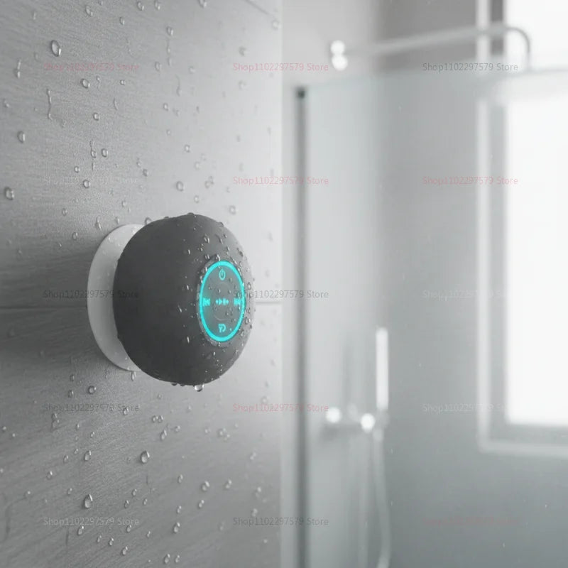 Grey, portable, waterproof Bluetooth speaker with a suction cup, featuring glowing blue LED controls on a tiled wall.