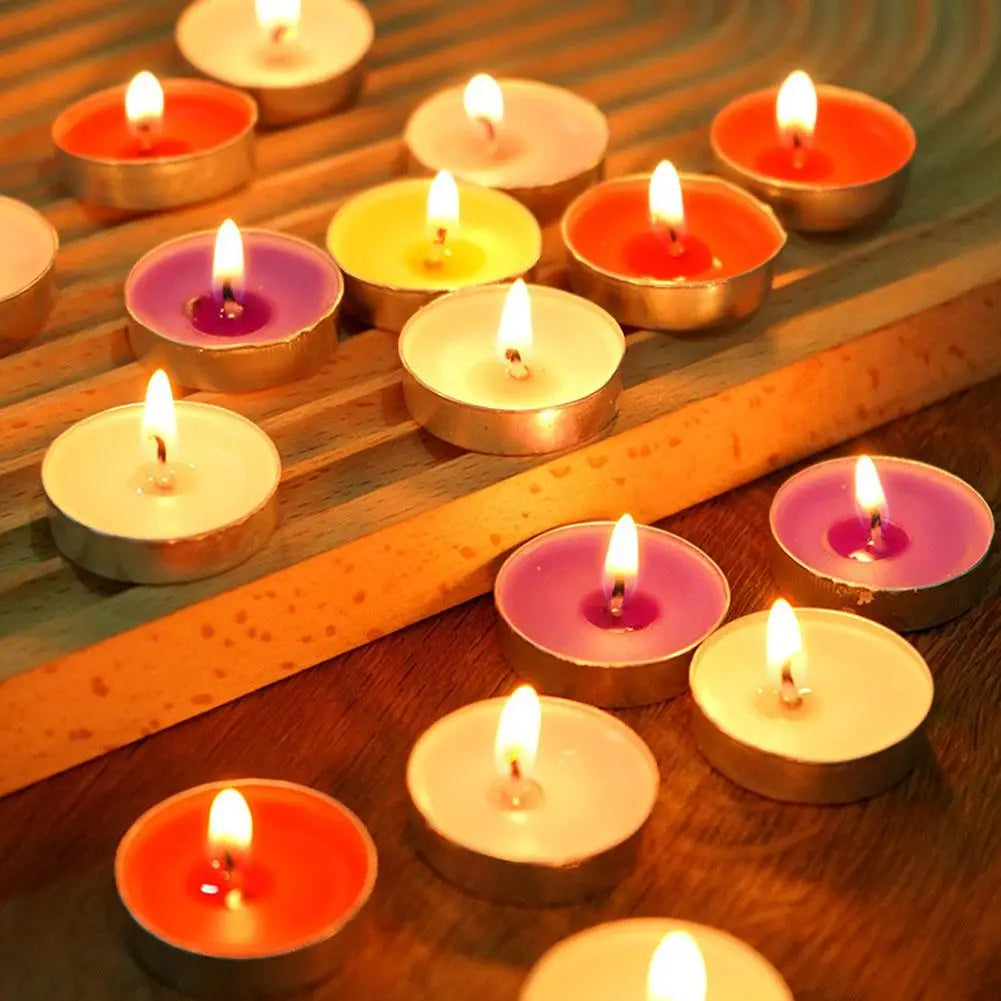 Assorted lit tea light candles in vibrant colours, each in a small metal casing, arranged on a wooden surface.