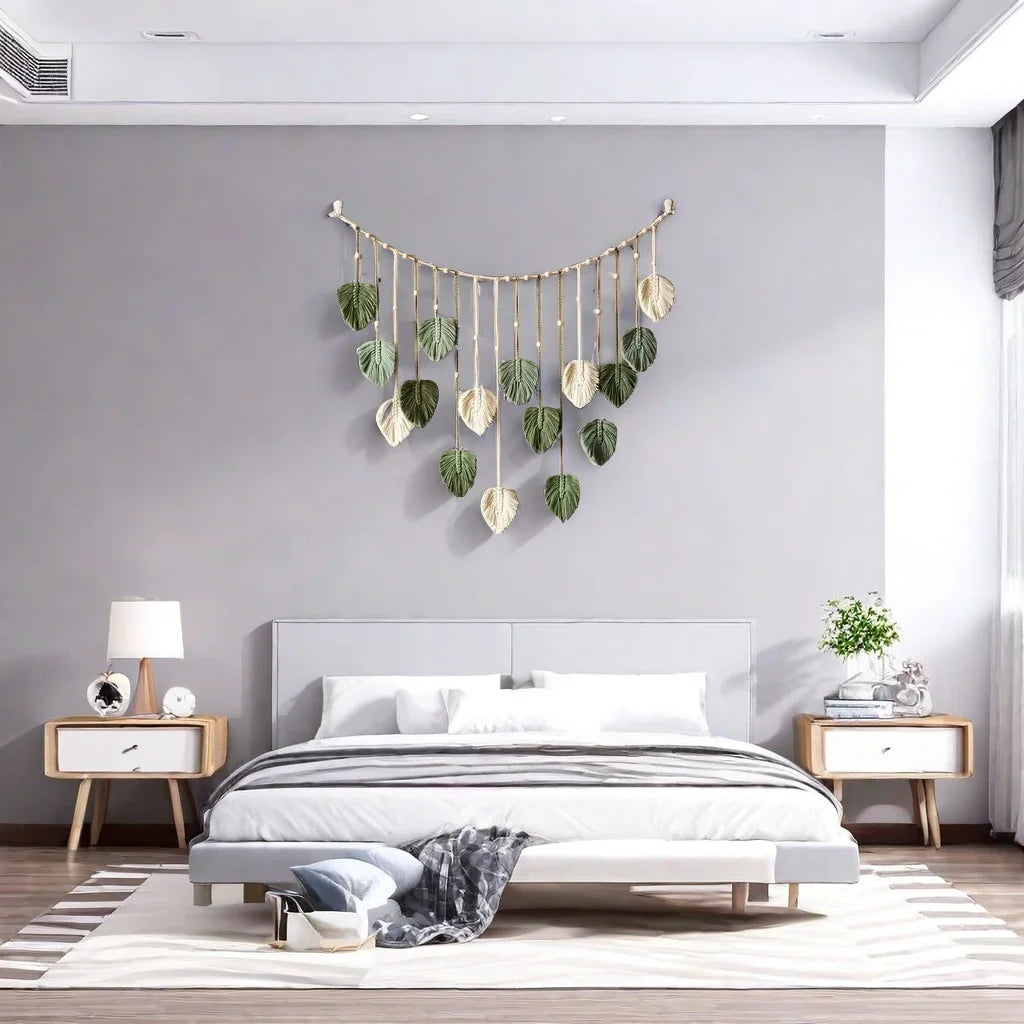 Boho macramé wall hanging featuring sage green and cream leaf-shaped tassels on a curved wooden branch.