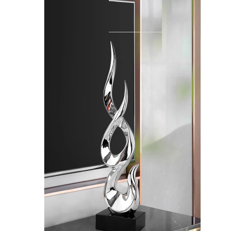 Tall, abstract silver-finish resin ornament with a sculptural flame-like design on a black rectangular base.