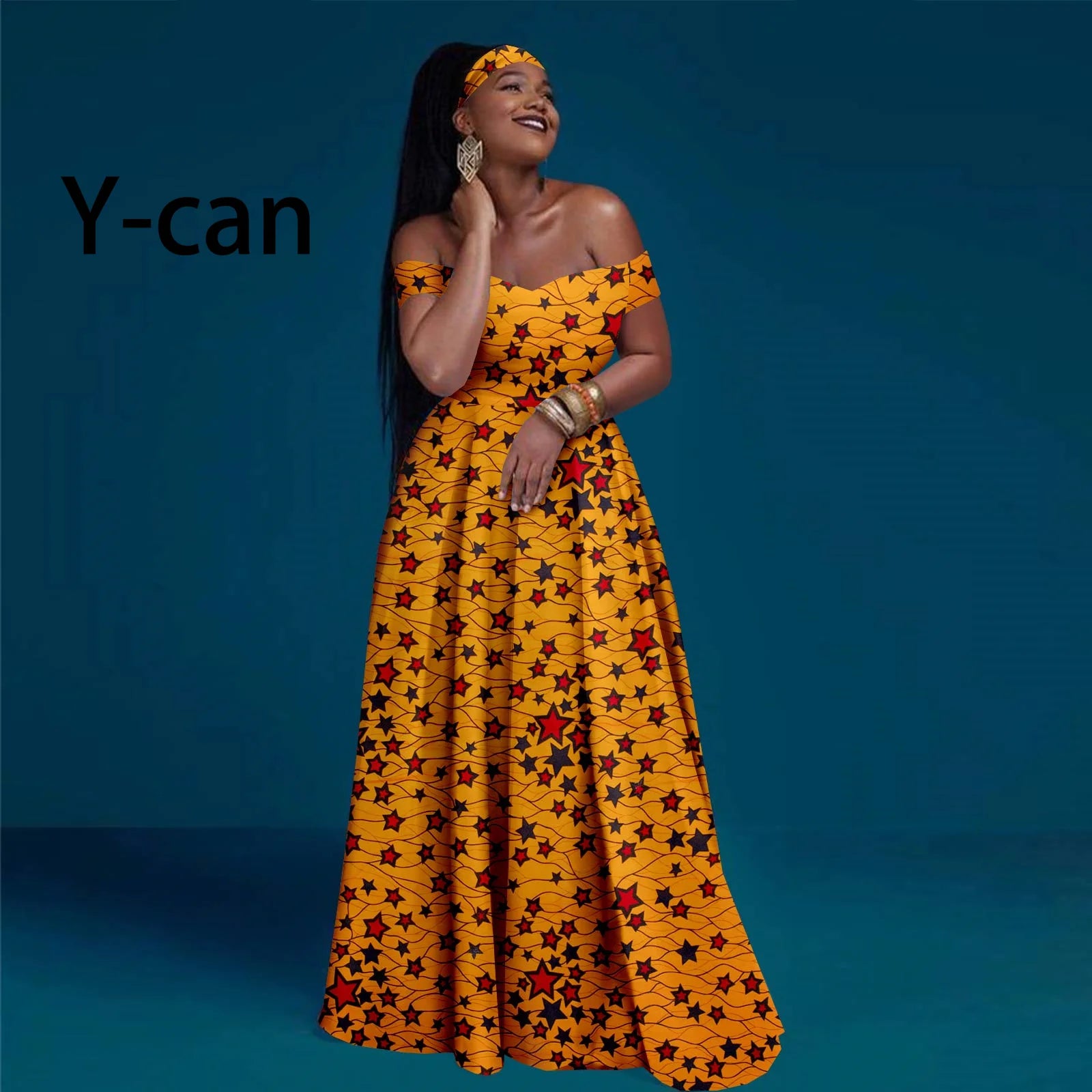 Model wearing a yellow off-shoulder maxi dress with a red and black star pattern and matching head wrap.