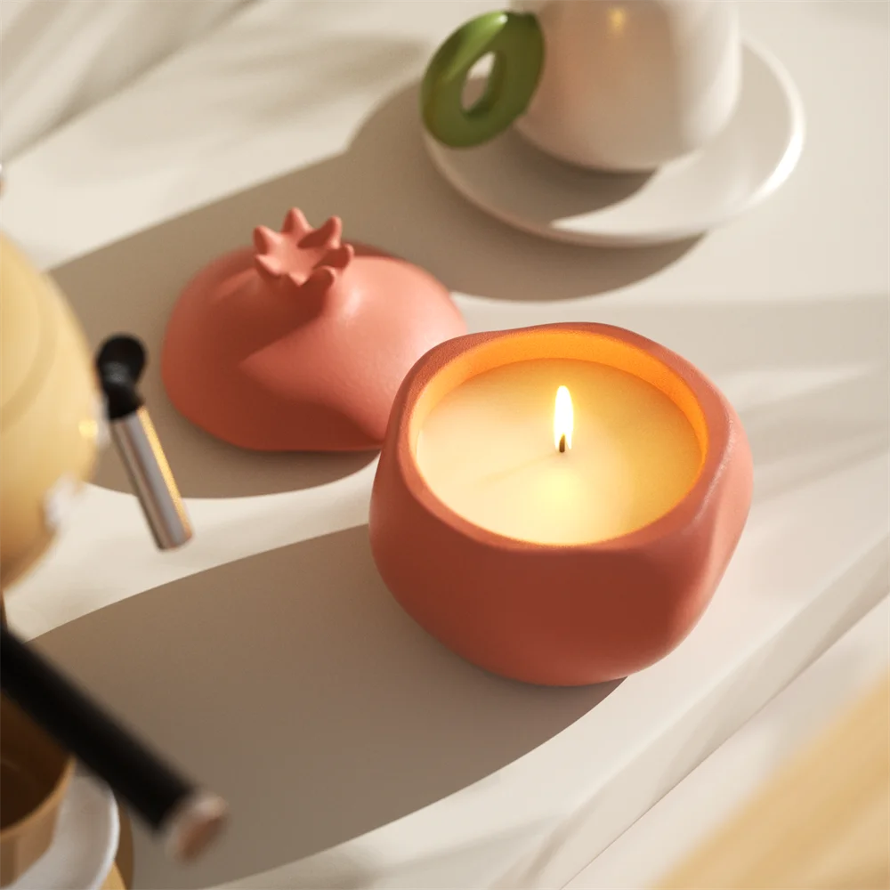 Coral pink pomegranate-shaped concrete candle jar with lit white wax and matching lid.