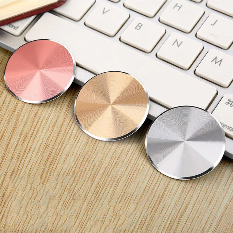 Three circular, metallic phone grips in rose gold, gold, and silver with a radial brushed texture on a desk.