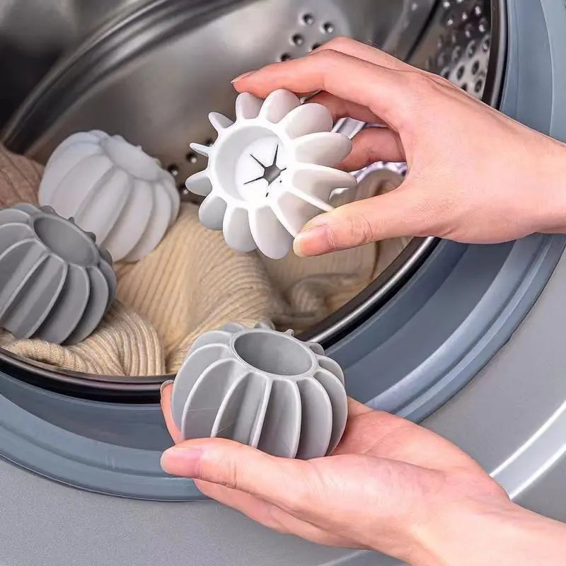 Hands holding grey and white ribbed, pumpkin-shaped laundry washing balls inside a tumble dryer drum with clothing.