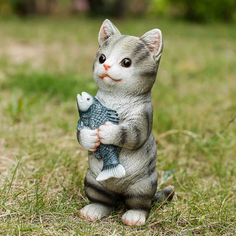 A charming resin garden ornament of a standing grey tabby kitten happily holding a fish.
