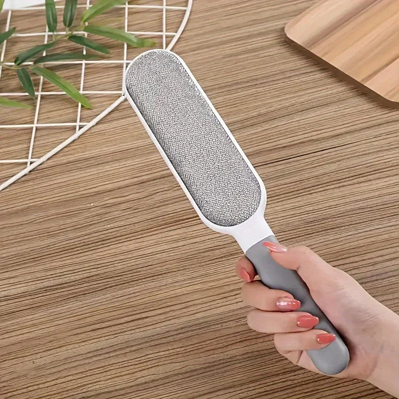 A hand holding a grey and white fabric lint remover brush on a wooden tabletop.