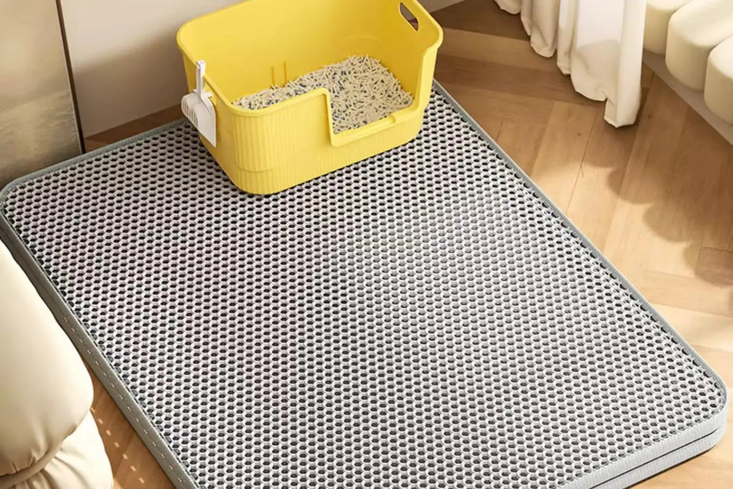 Grey honeycomb-textured waterproof cat litter mat on a wooden floor, with a yellow litter tray placed on top.