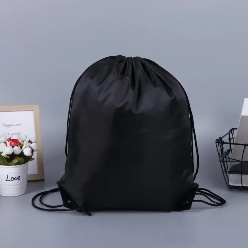 Plain black drawstring bag with adjustable rope straps, set against a grey background.