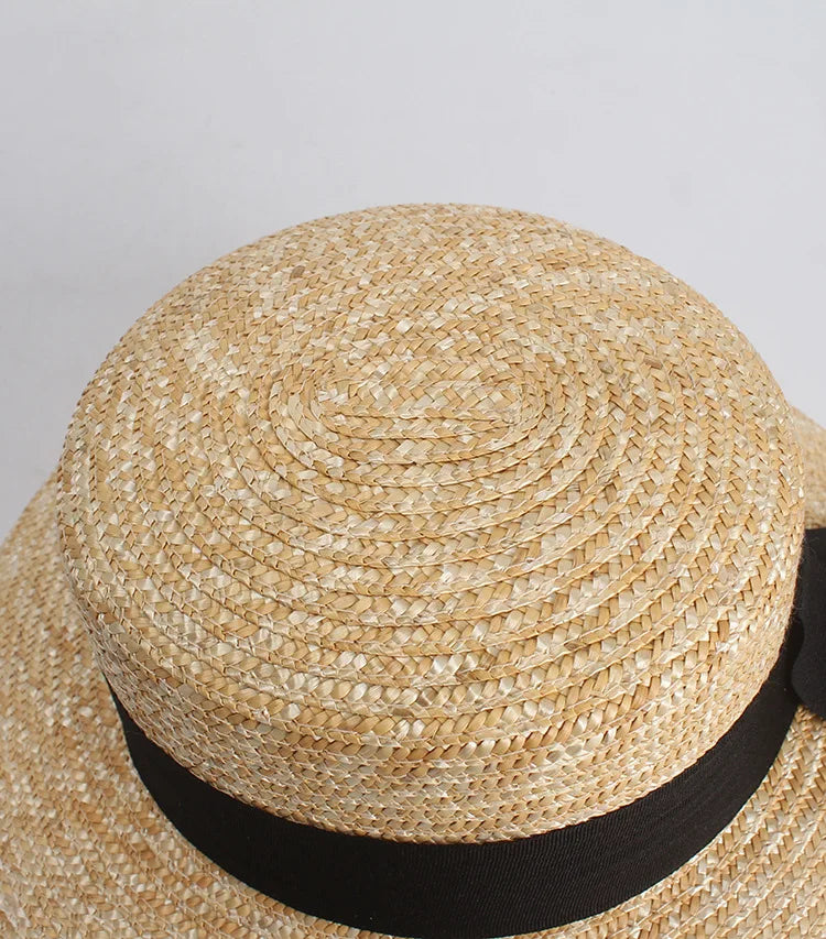 Top-down view of a natural straw sun hat with a flat crown, wide brim, and elegant black ribbon band.