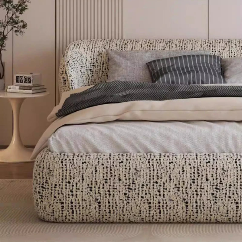 Modern bed frame with a curved, chunky headboard in a cream and black speckled textured fabric.