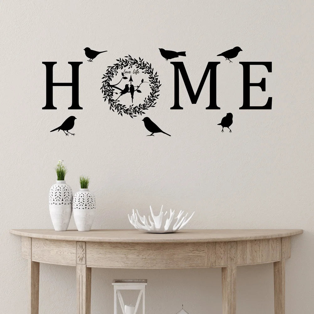 Black self-adhesive wall sticker spelling 'HOME', with an 'O' shaped as a floral wreath and silhouettes of birds.