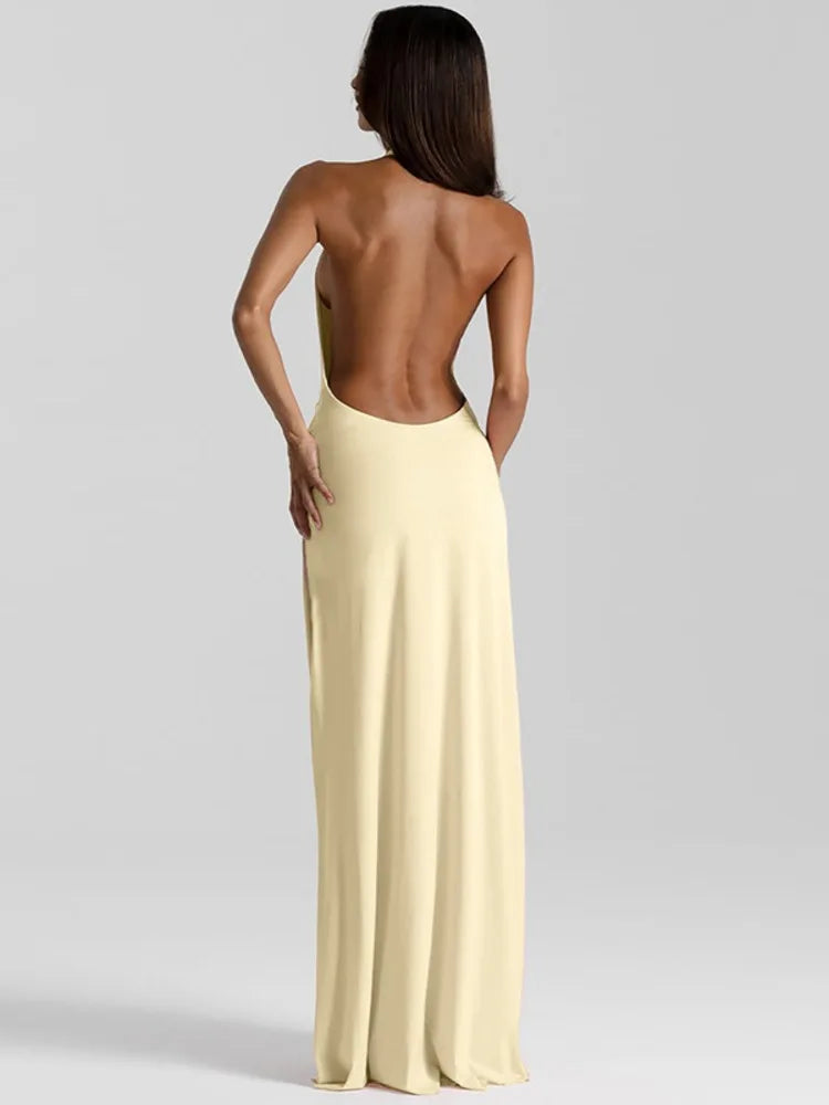Pale yellow backless maxi dress with a halter neckline, sleeveless cut, and a high thigh split.