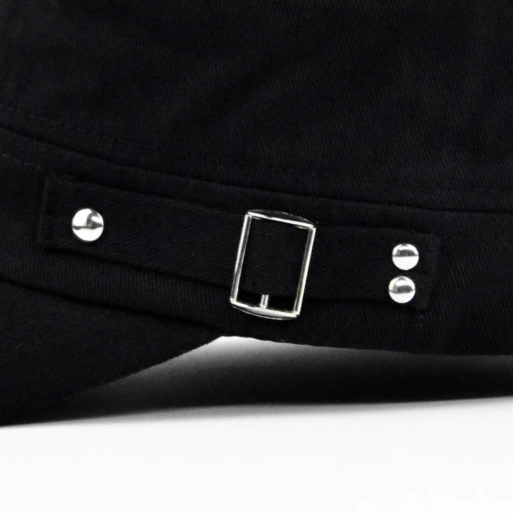 Close-up of a black military-style cap featuring a decorative fabric strap with a silver buckle and rivet details.