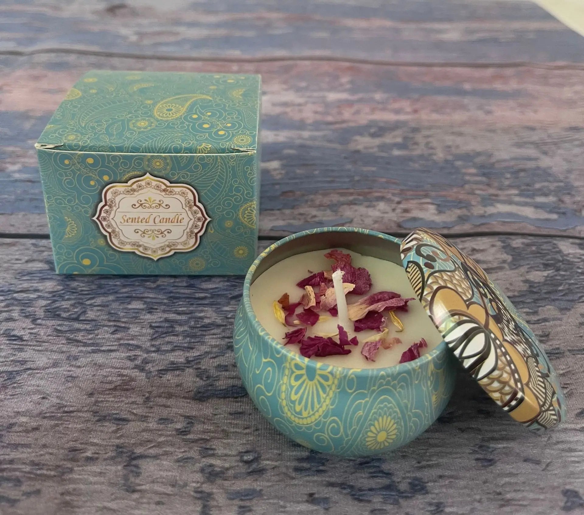 Teal paisley scented candle in a decorative tin with dried flower petals, next to its matching patterned gift box.