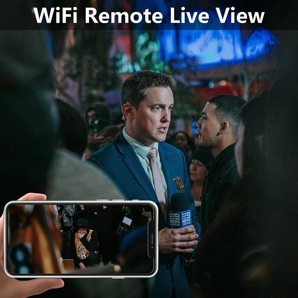 Small black plastic clip-on spy camera attached to a suit jacket, showing a live video feed on a smartphone screen.