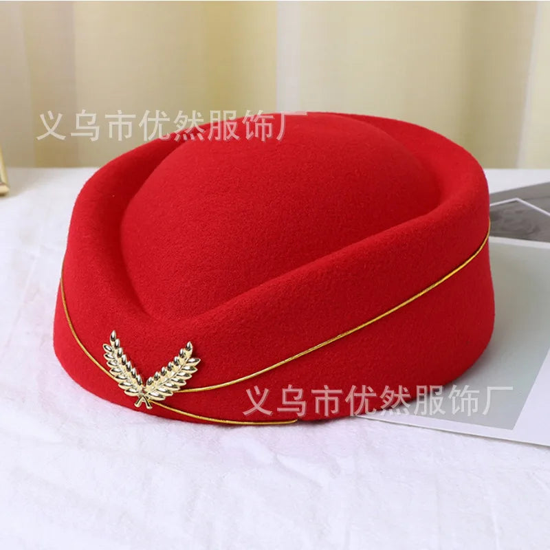 Bright red felt pillbox hat featuring gold trim and a metallic laurel leaf emblem on the front.