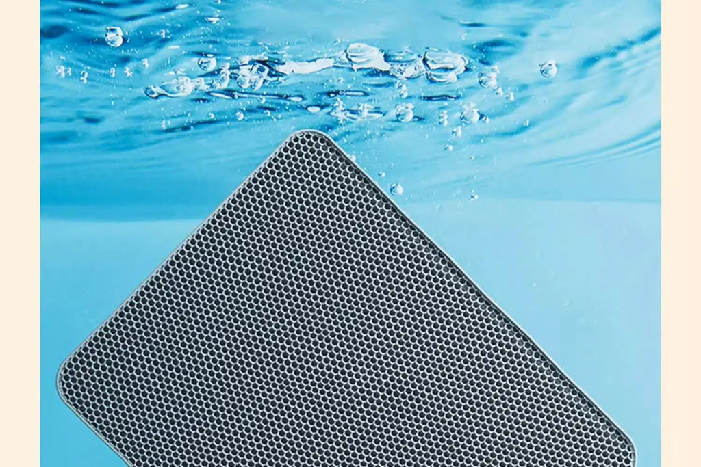 Grey, waterproof cat litter mat with a honeycomb design, submerged in water to demonstrate its durability.